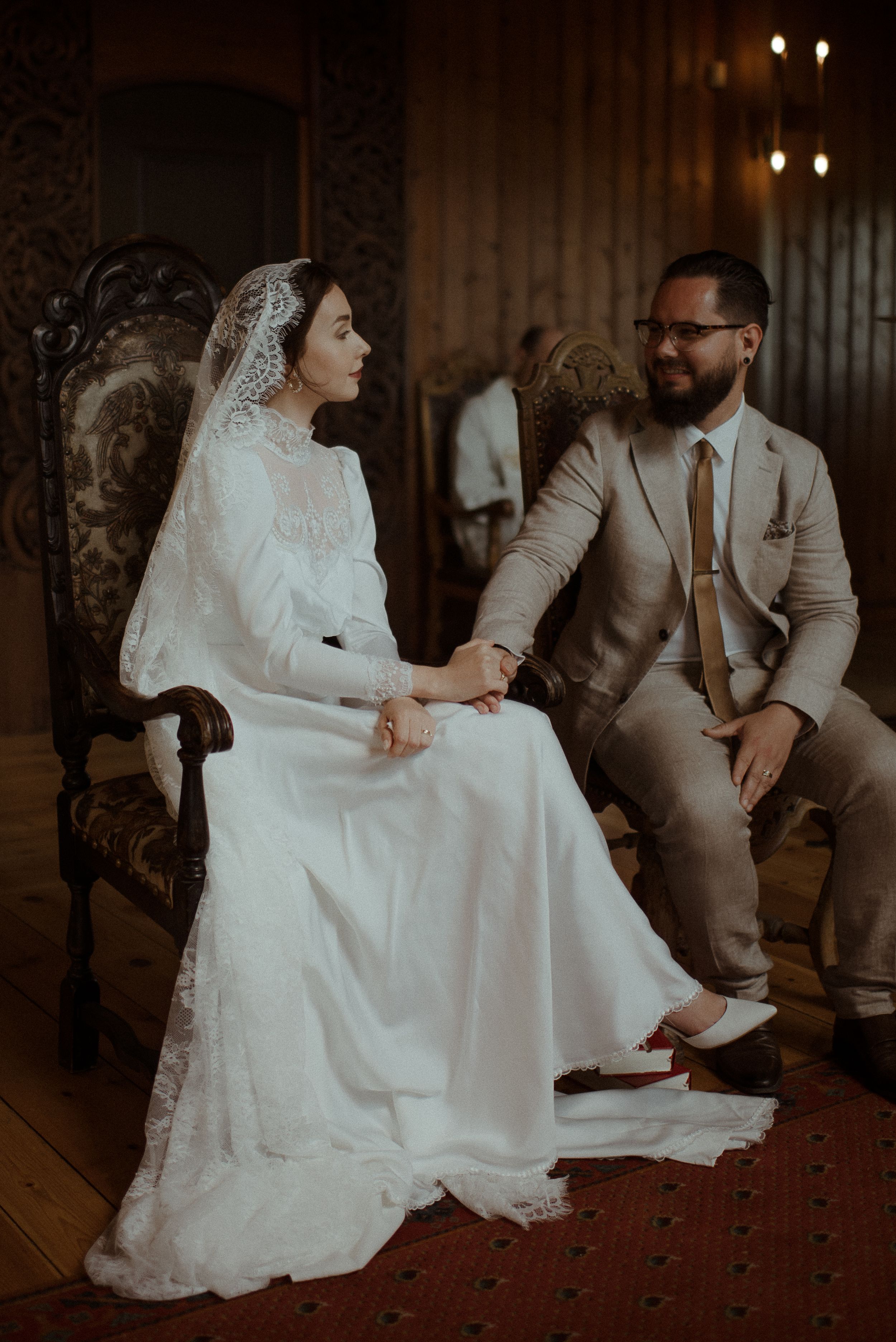 A tender wedding moment captured on an ornate antique chair in moody lighting.