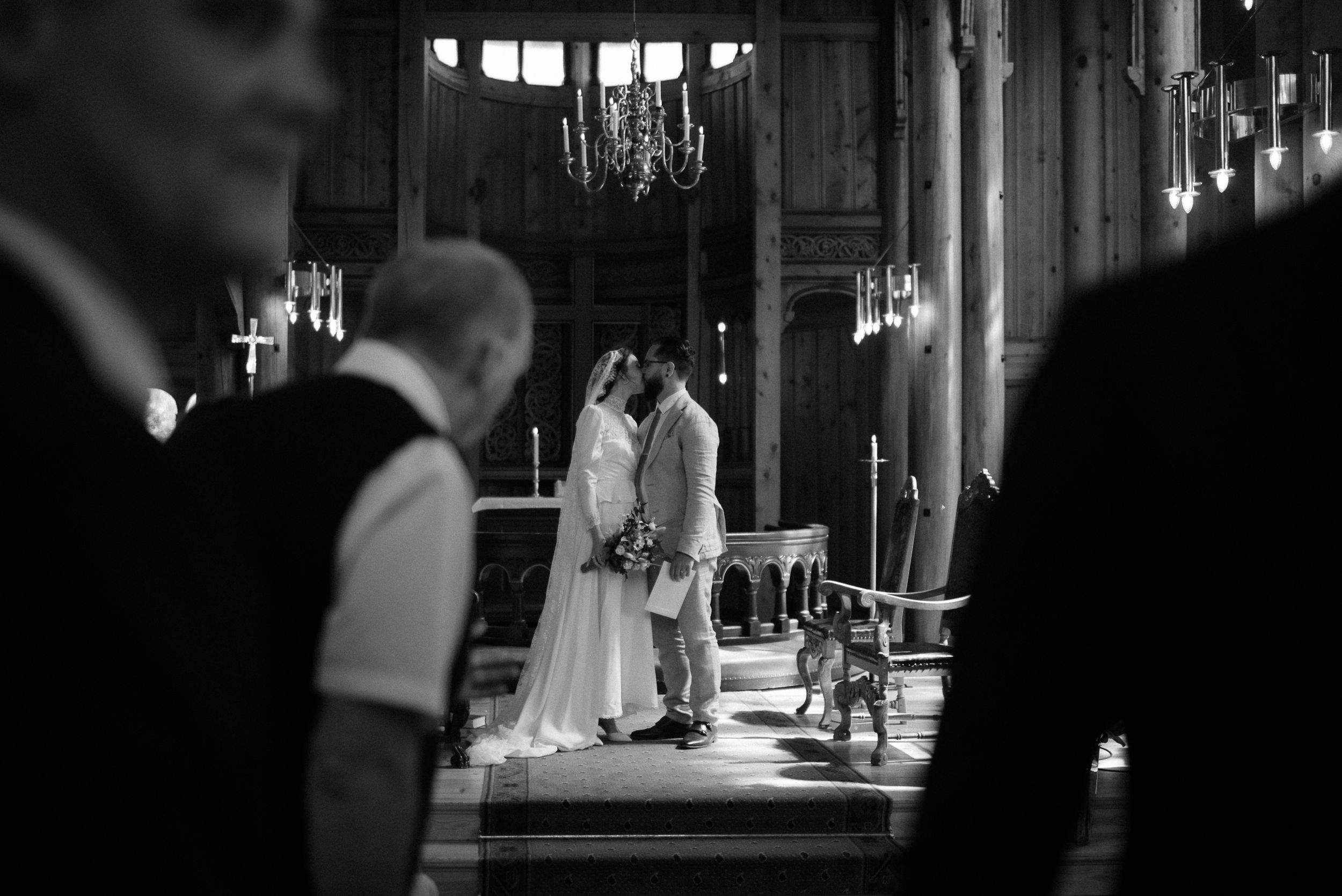A black and white photograph of a wedding ceremony in a historic church with chandeliers.