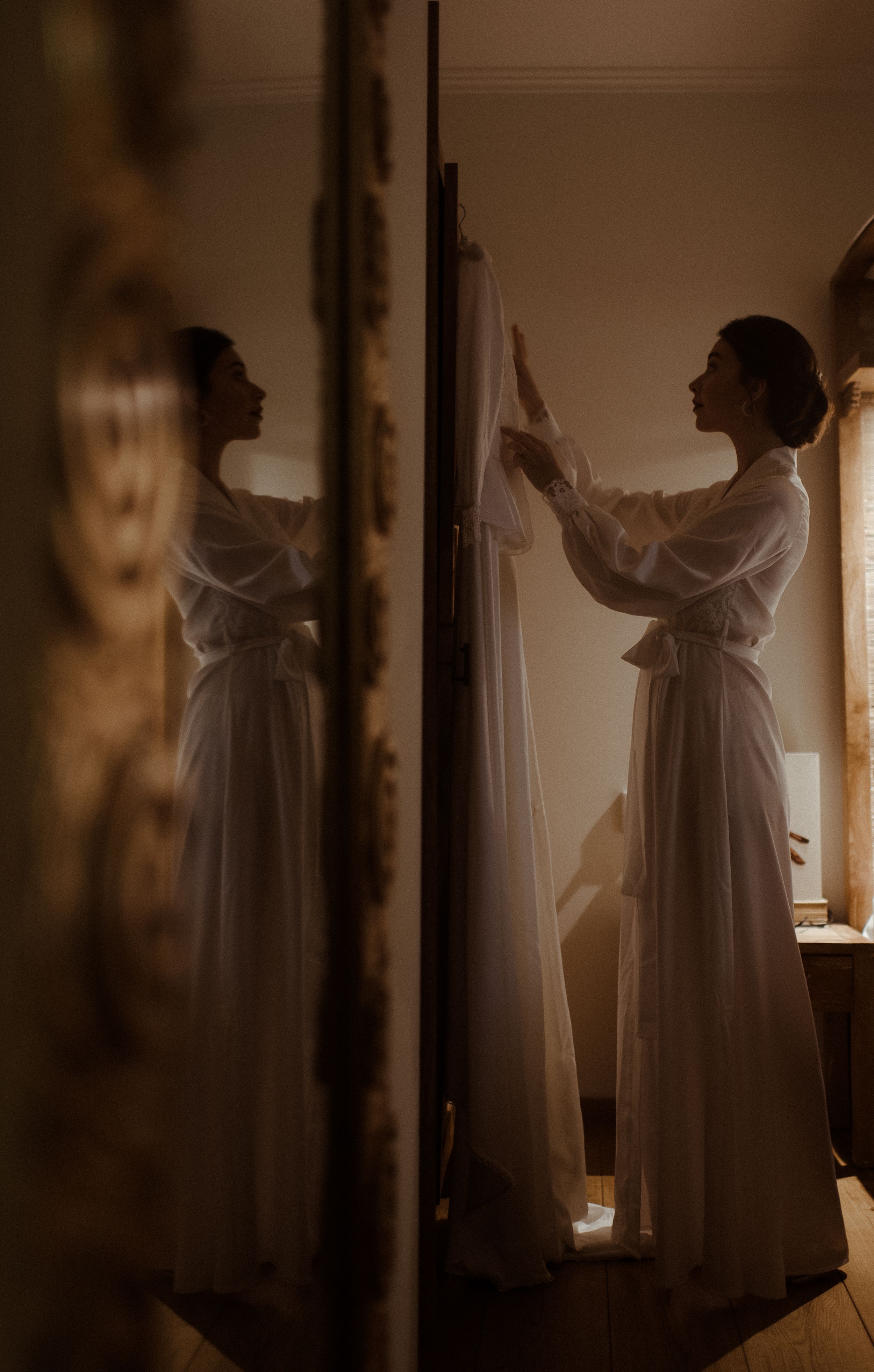 Atmospheric mirror reflection shot of figure in flowing white dress in warm lighting.