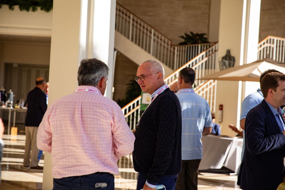 Attendees in business casual attire engage in conversation during a networking event near a grand staircase.