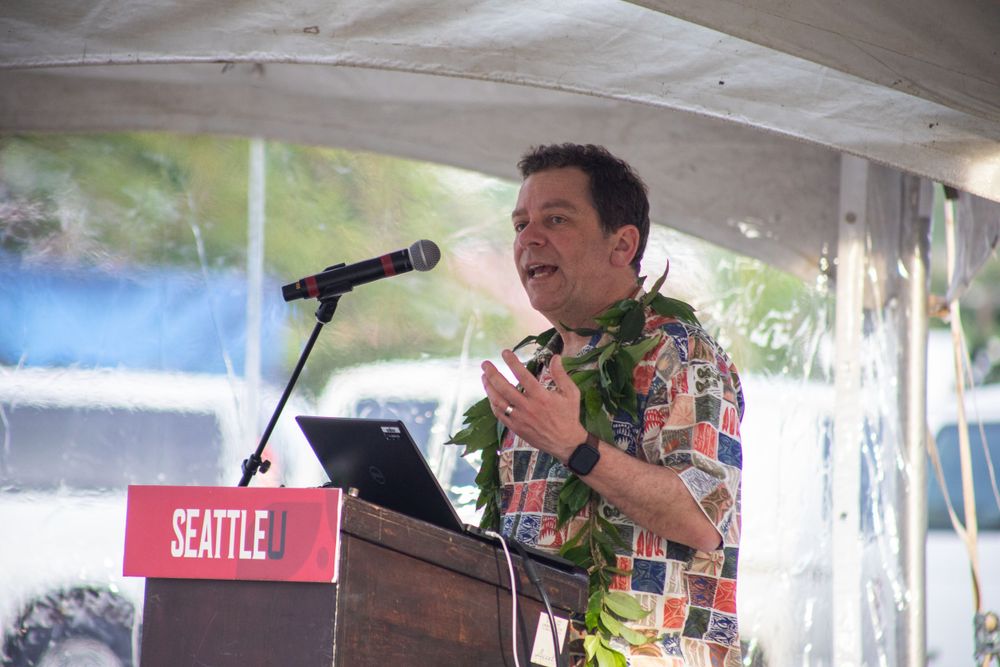 A speaker in a Hawaiian shirt addresses an audience at an outdoor event in Seattle.