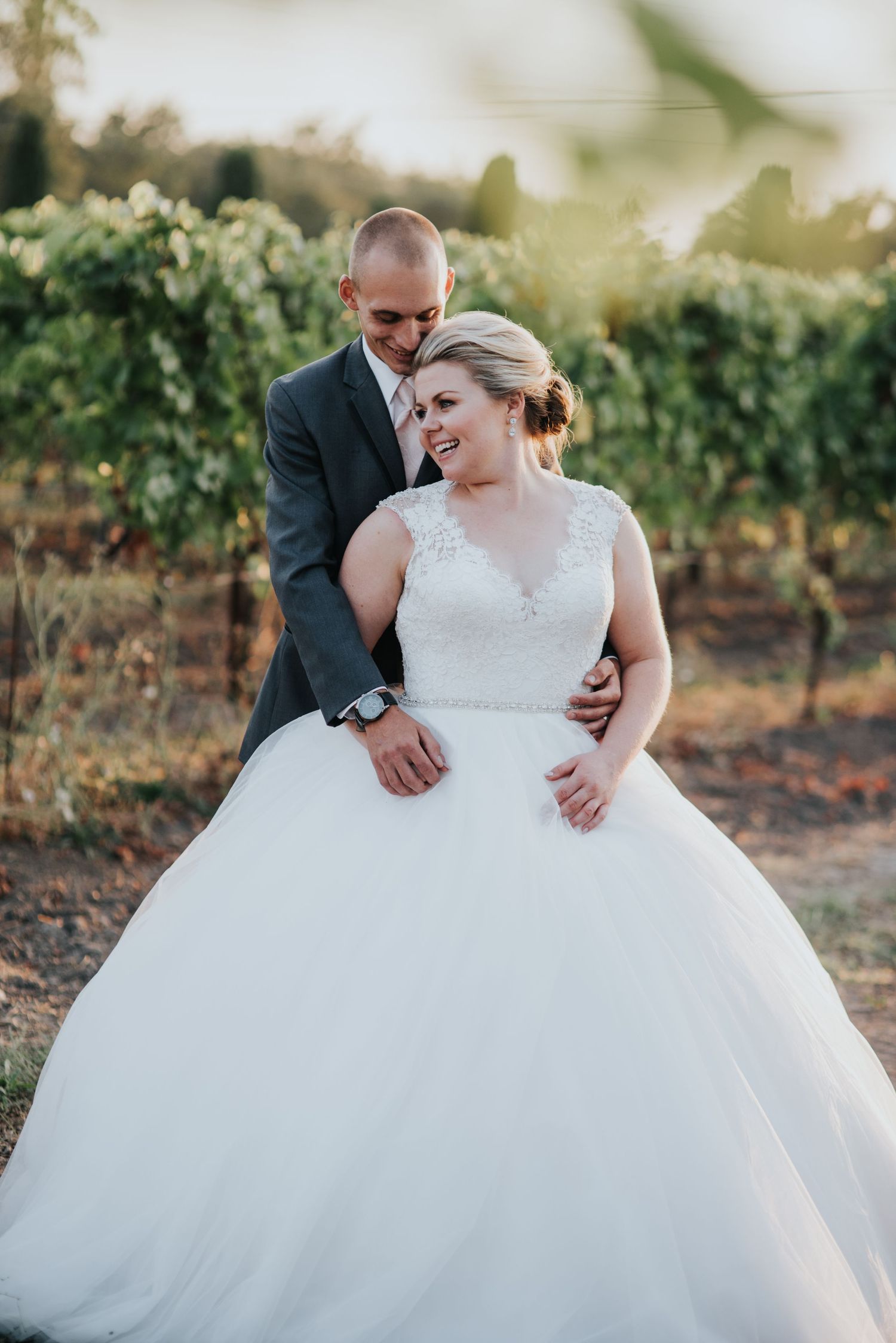 Elegant bride in a classic ballgown standing in Vintners inn, beaming with joy as the golden hour light filters through the grapevines.