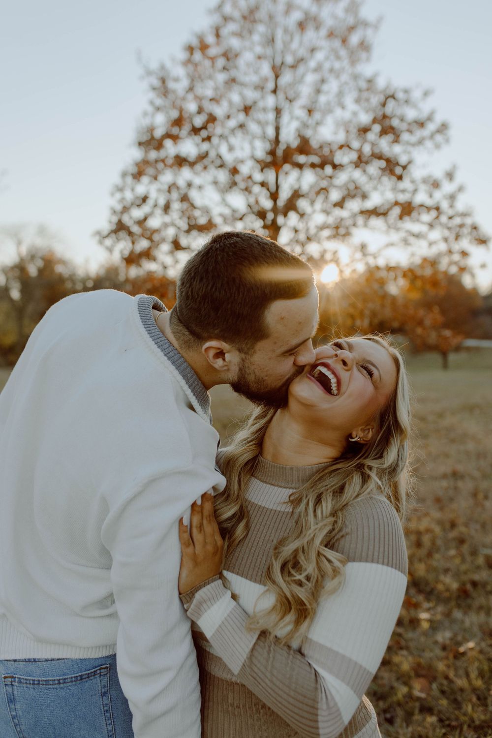 A couple shares a romantic moment laughing together in warm sunlight during an outdoor autumn photoshoot.