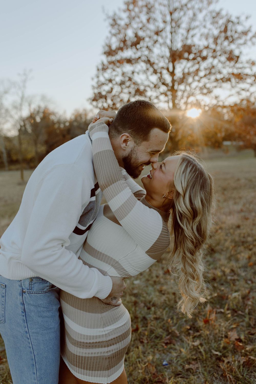 Romantic couple in cozy sweaters share an intimate moment at sunset in an autumn field with golden light.