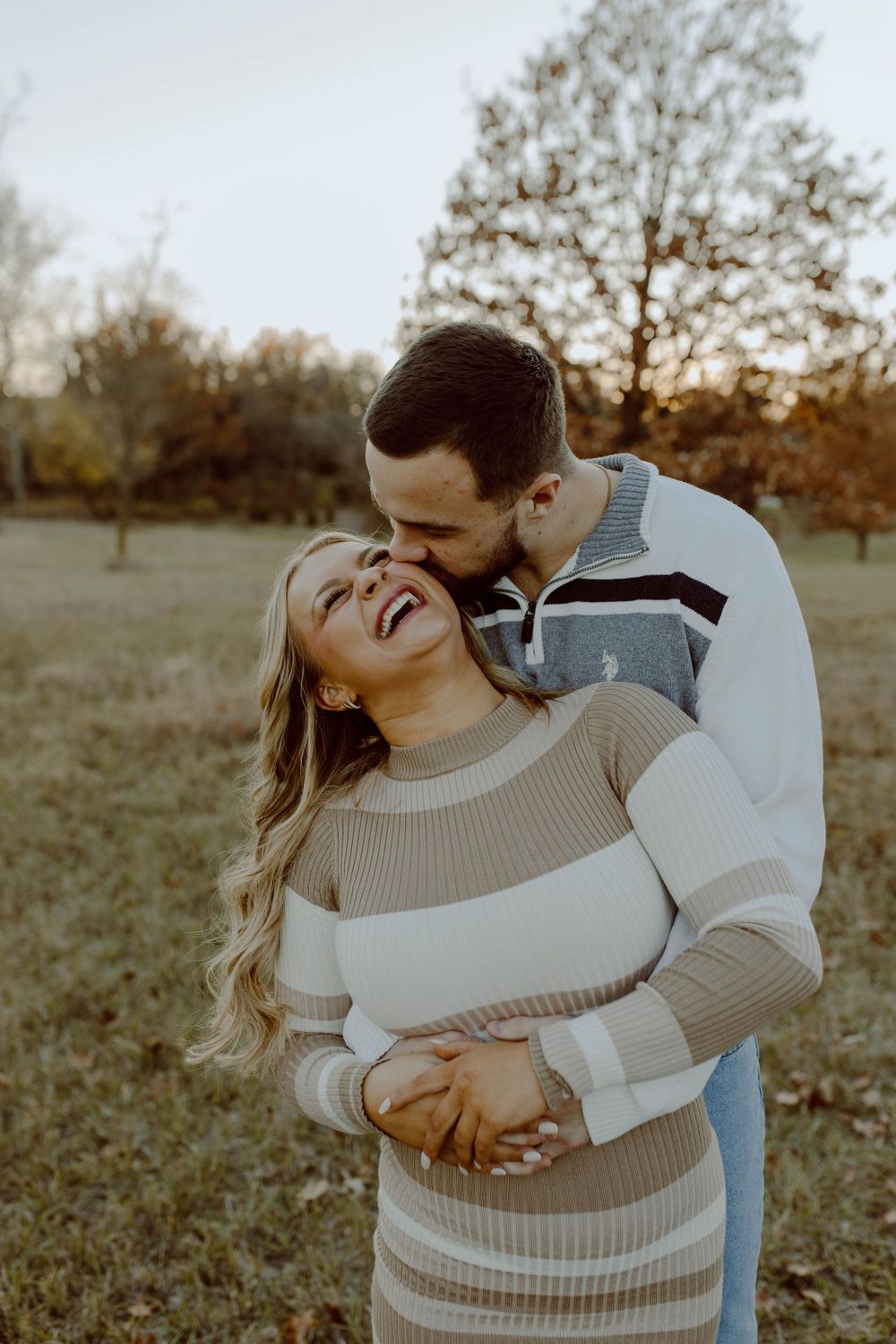 A couple shares a tender embrace outdoors during golden hour while wearing cozy sweaters in autumn.