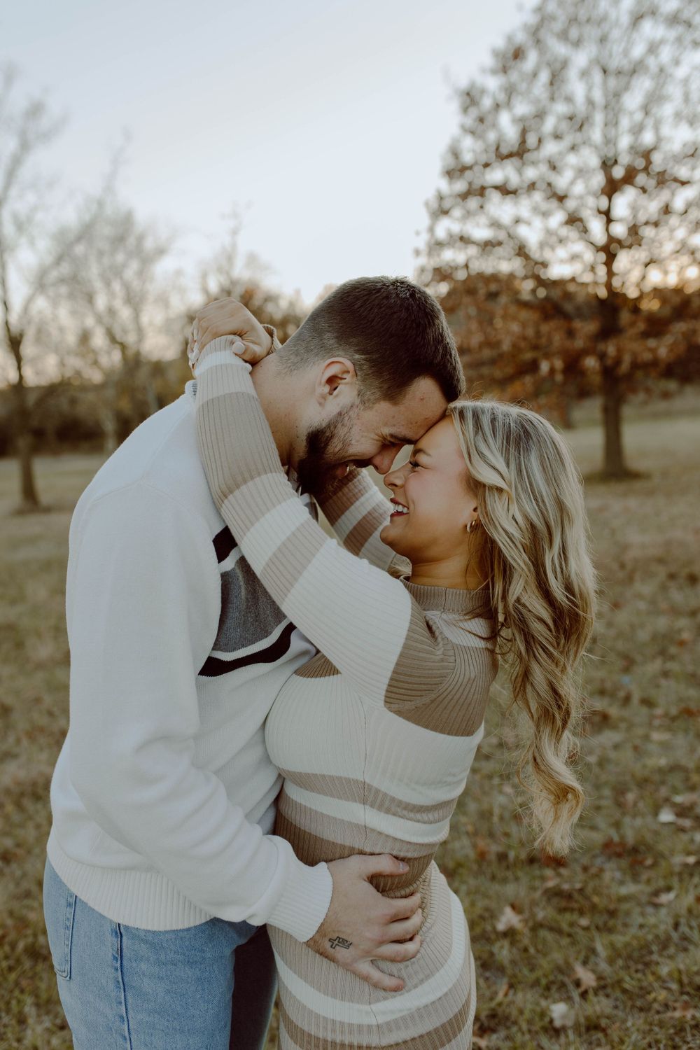 Romantic golden hour portrait of couple in matching beige sweaters embracing outdoors in autumn setting.