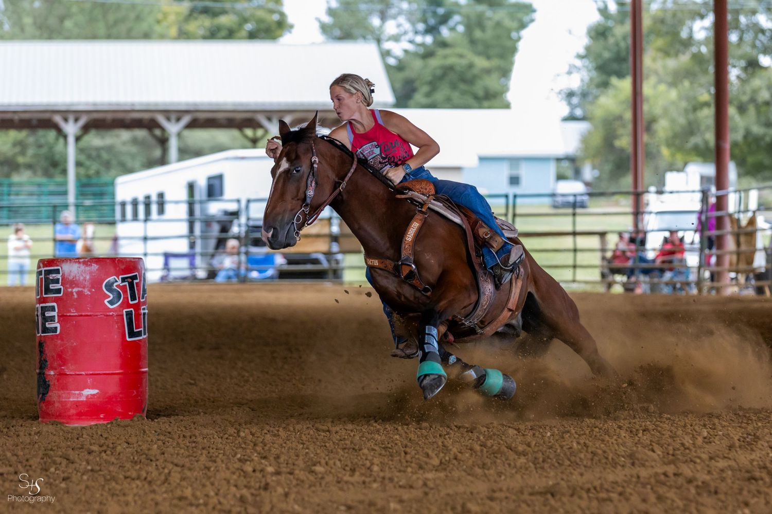 Barrel racing action shot with horse and rider making sharp turn in dirt arena.