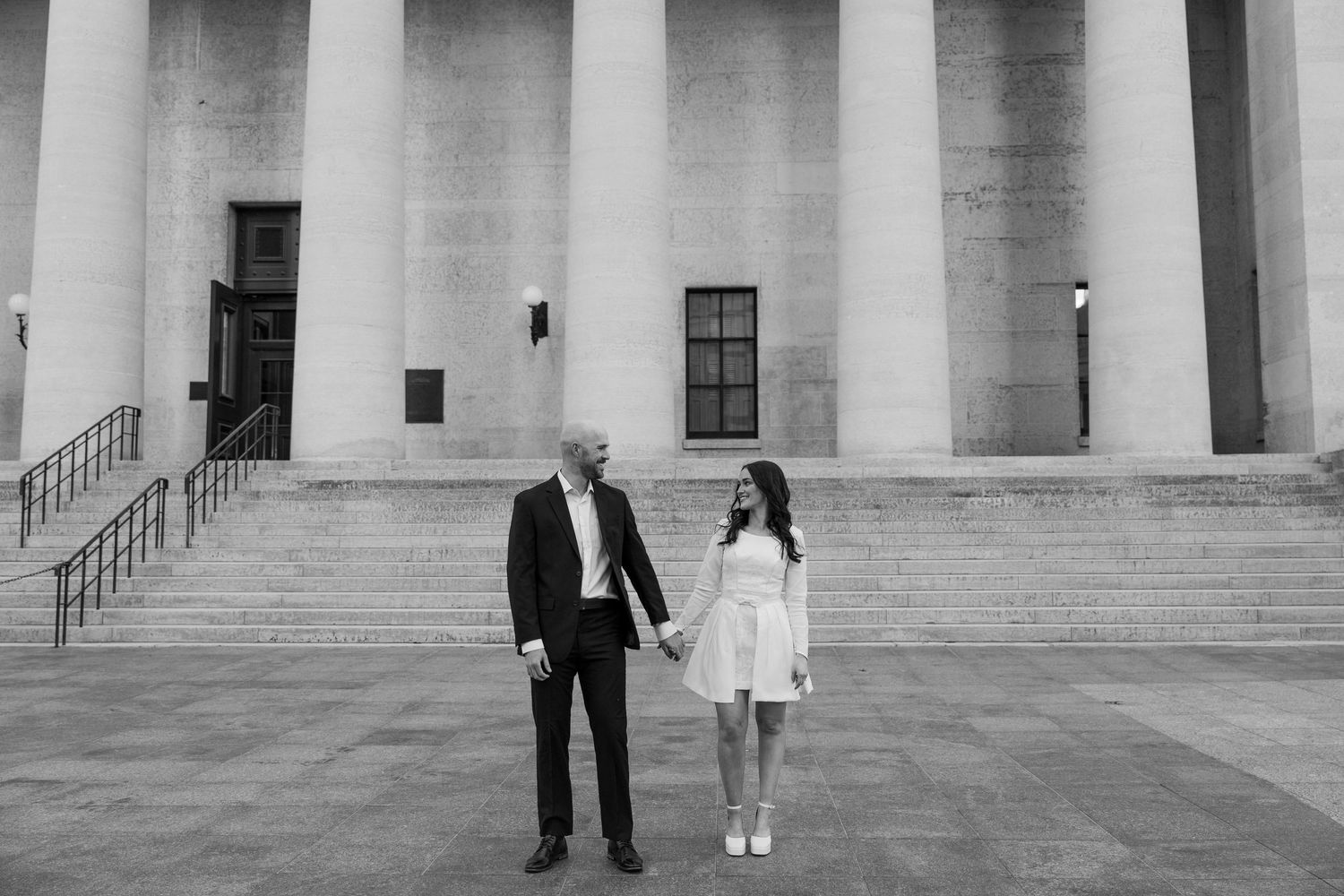 Couple photographed in black and white standing in front of grand columns of a historic building.