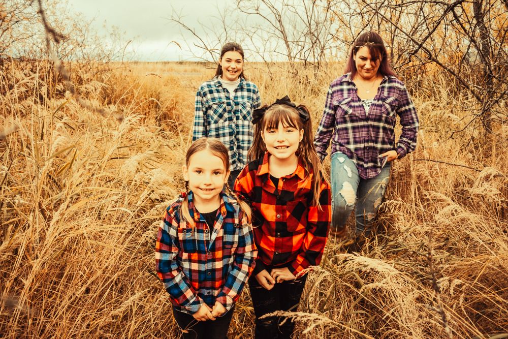Four people wearing coordinated plaid flannel shirts pose together in a field of tall golden grass.
