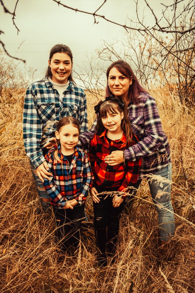 A family in matching plaid flannel shirts stands together among autumn prairie grass.