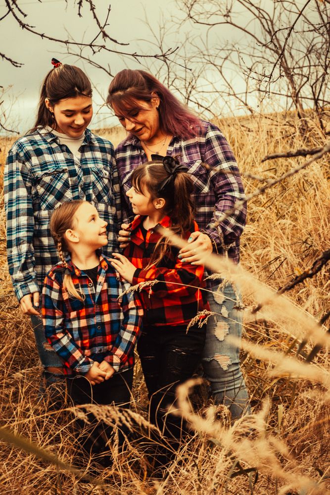 A candid family moment captured in tall grass wearing coordinating buffalo plaid shirts.