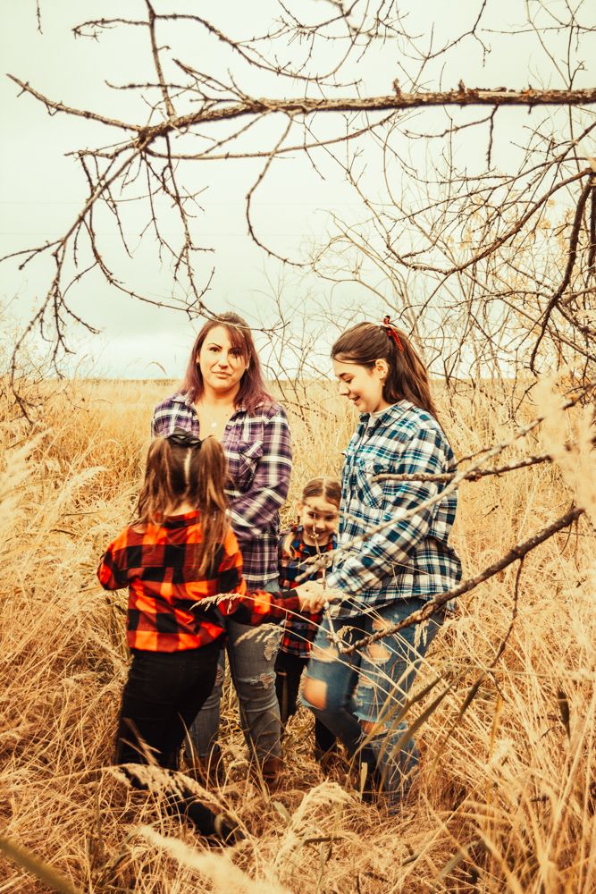 Three people in plaid flannel shirts stand together in tall golden grass during autumn.