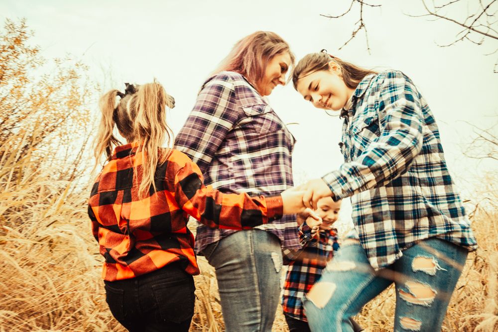 Three people share a playful moment while wearing coordinated plaid shirts in a prairie setting.
