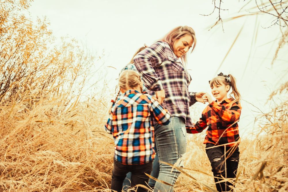 Three people in matching buffalo plaid shirts share a candid moment in tall prairie grass.