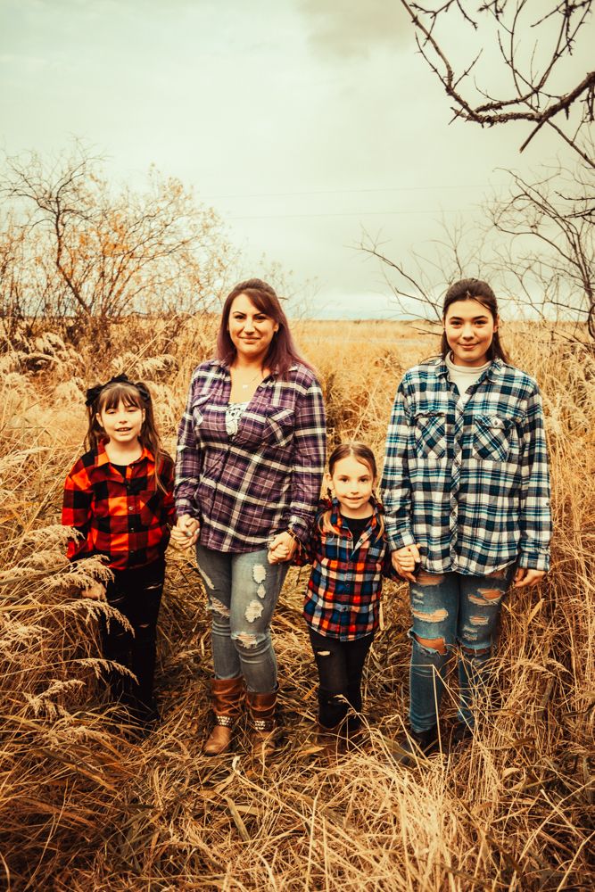 Four people line up in matching plaid flannel shirts against a backdrop of autumn prairie grass.