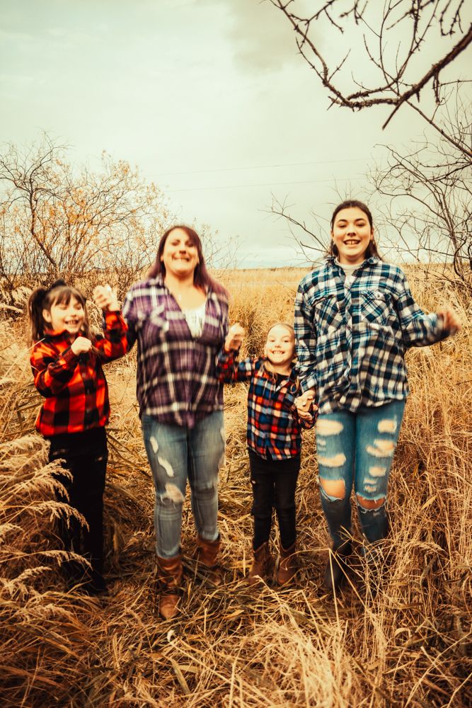 Four people in coordinated plaid shirts jump joyfully in a field of tall grass.