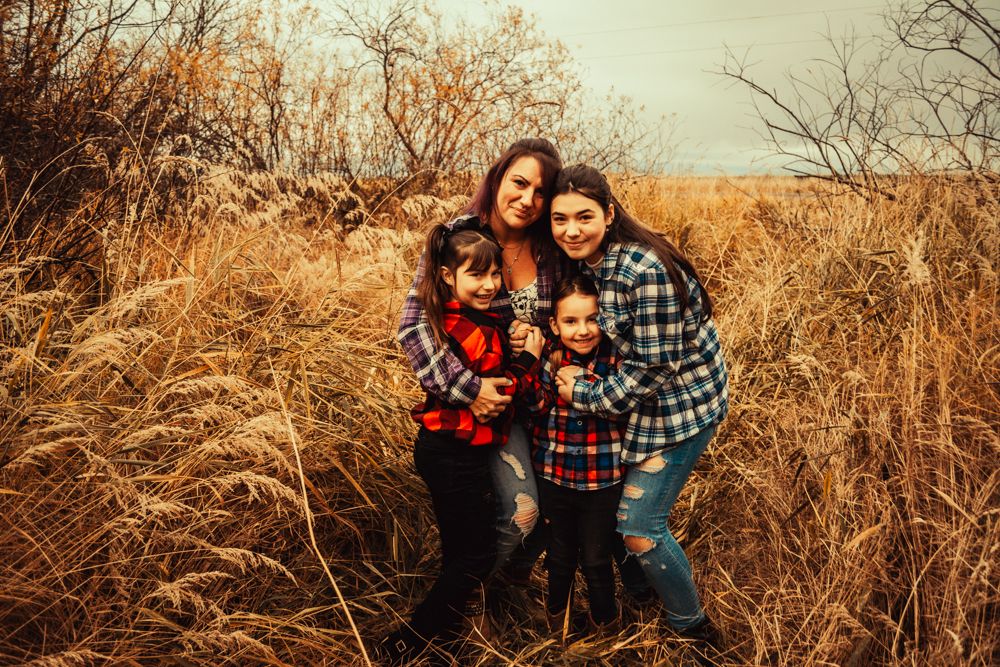 A family group poses closely together wearing matching plaid shirts in golden prairie grass.