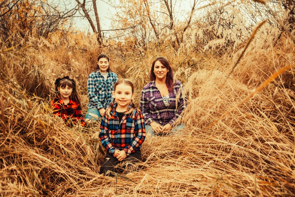 A warm-toned portrait of a group lying in tall golden grass wearing coordinated plaid shirts.