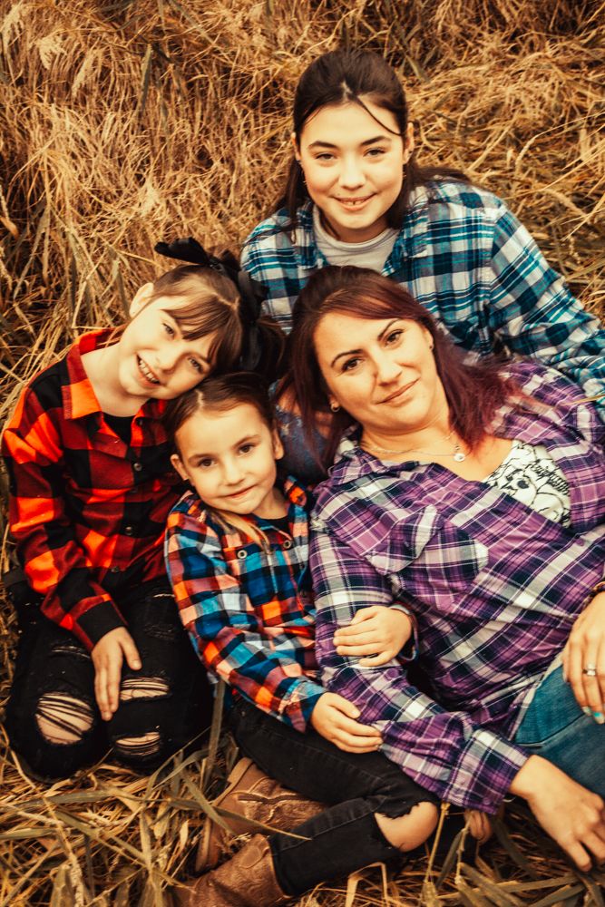 Candid family portrait with everyone wearing matching plaid shirts while relaxing in dried grass.
