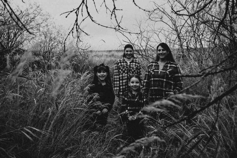 Family wearing plaid shirts poses in tall grass field.
