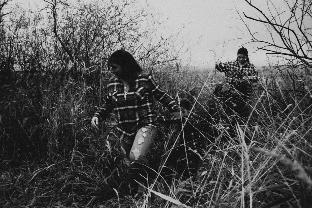 People in plaid jackets walking through tall grass and bare branches in black and white.