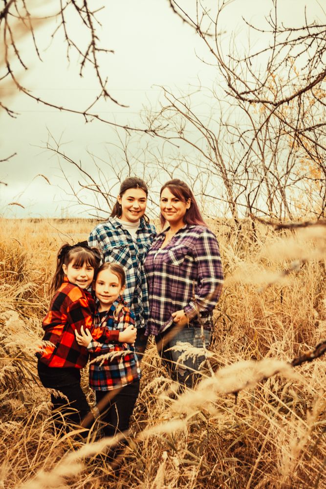 Family wearing plaid flannel shirts poses together in autumn field.
