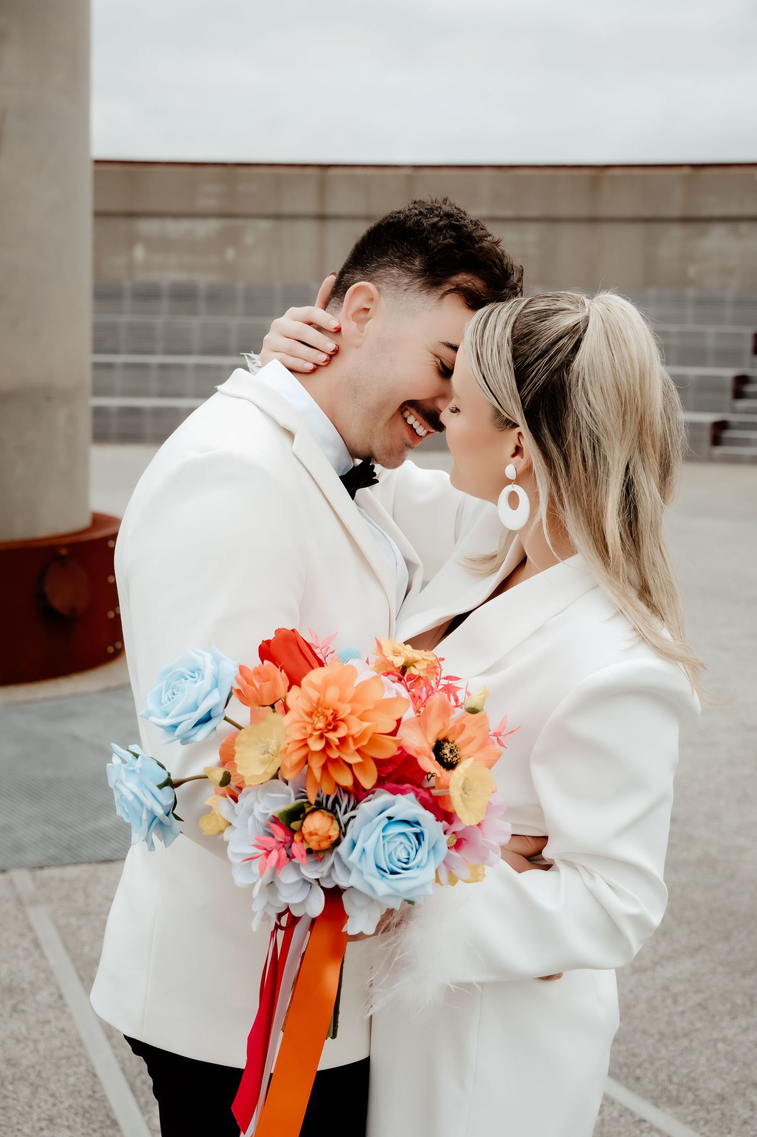 Modern wedding portrait with colorful bouquet featuring blue roses and coral flowers.