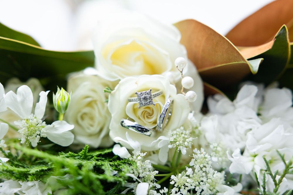 Close-up of white roses and wedding rings in a bridal bouquet arrangement.