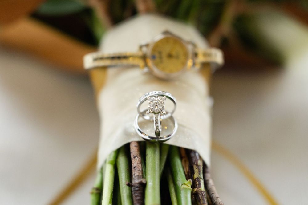 Wedding rings displayed on wrapped green flower stems with soft focus background.