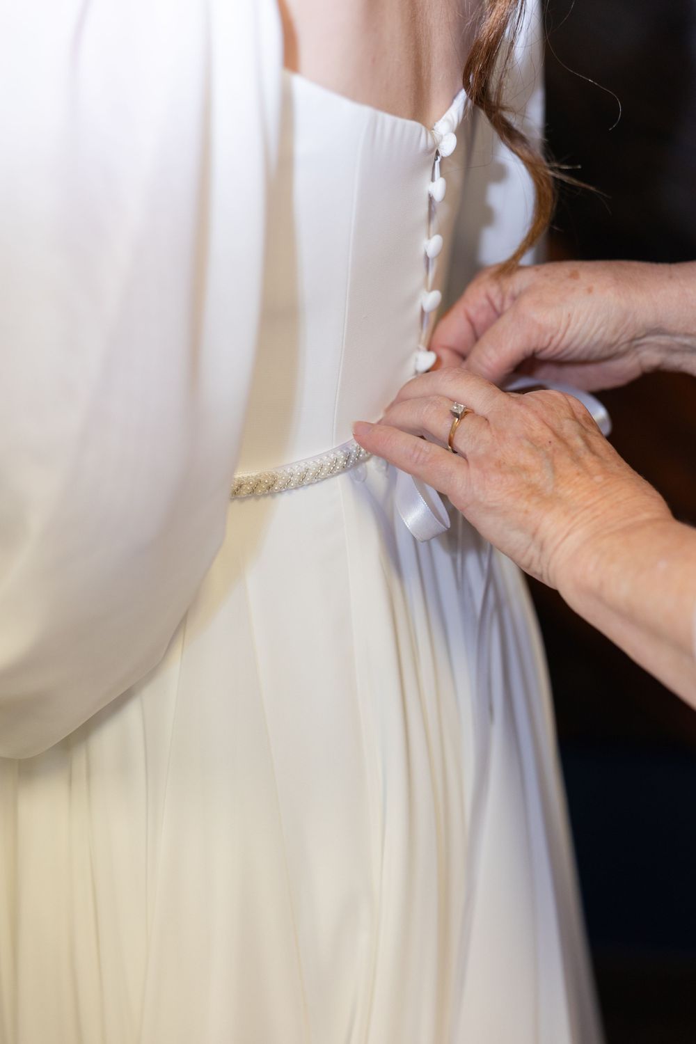 Close-up detail of hands adjusting a white wedding dress sash.