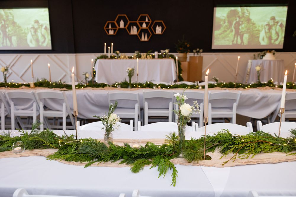 Wedding reception setup with white chairs, evergreen garland, and projector screens.