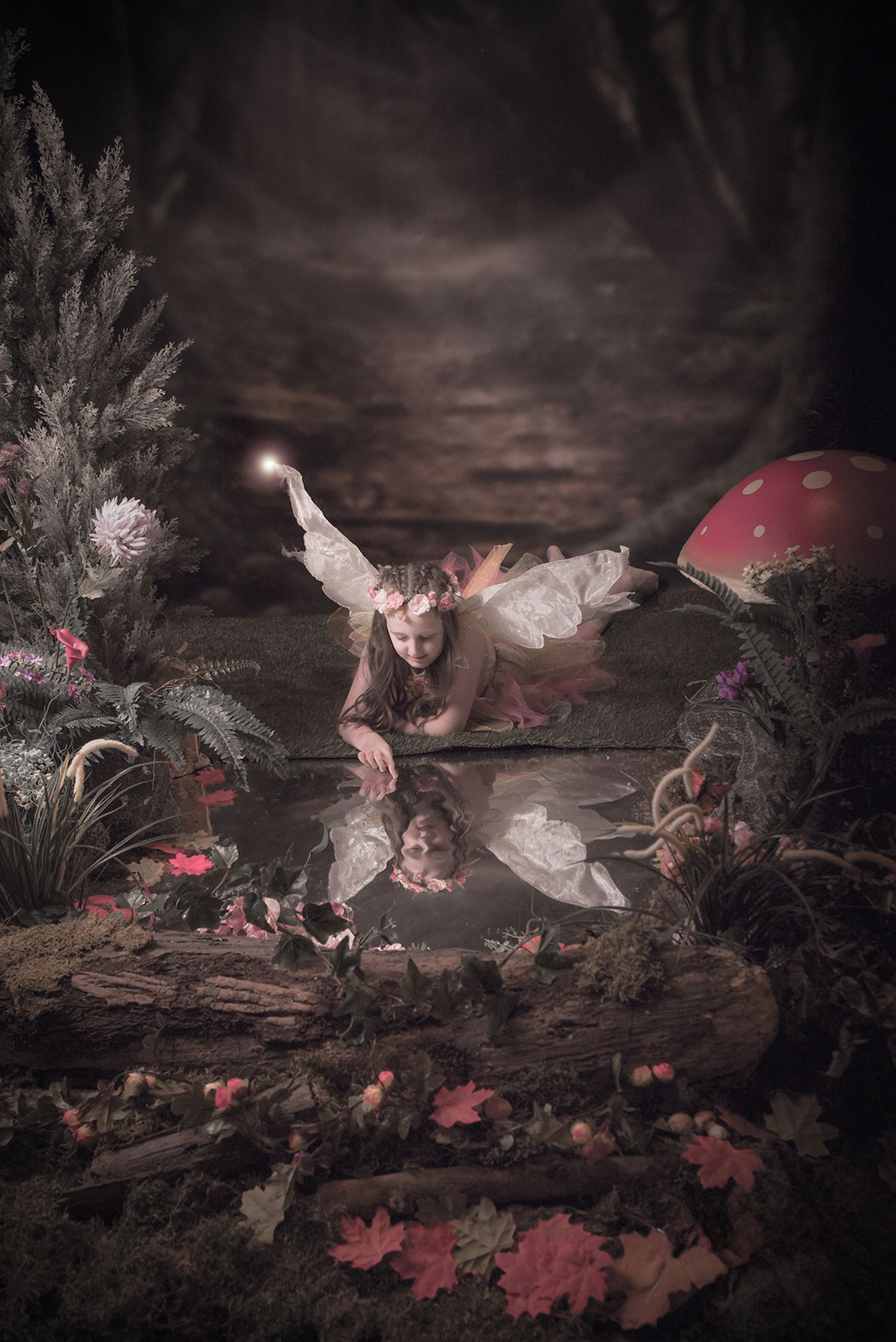 A fairy with delicate wings gazes at their reflection in a magical forest pond surrounded by flowers.