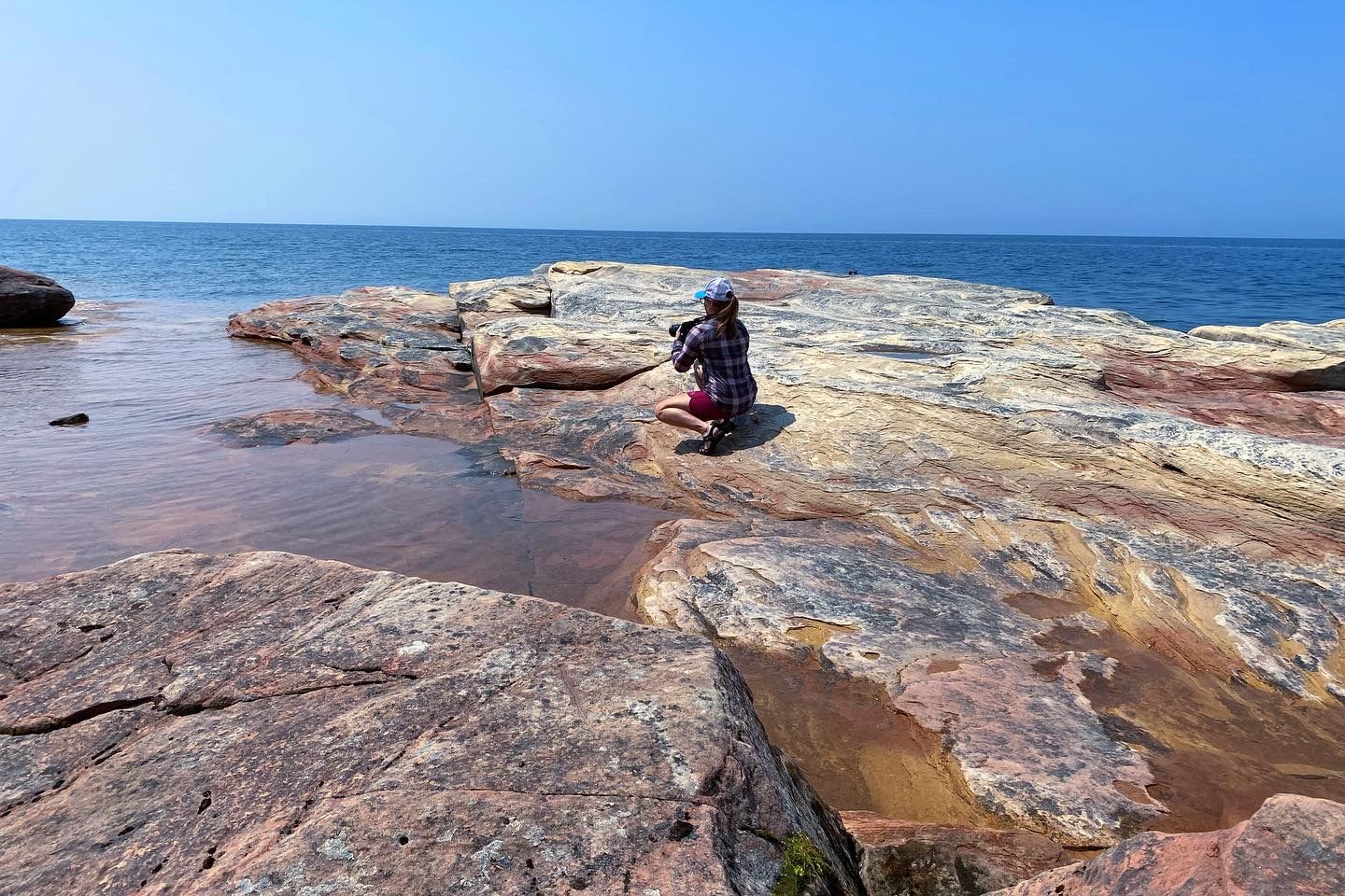 Picture of a woman with a camera on some rocks surrounded by water