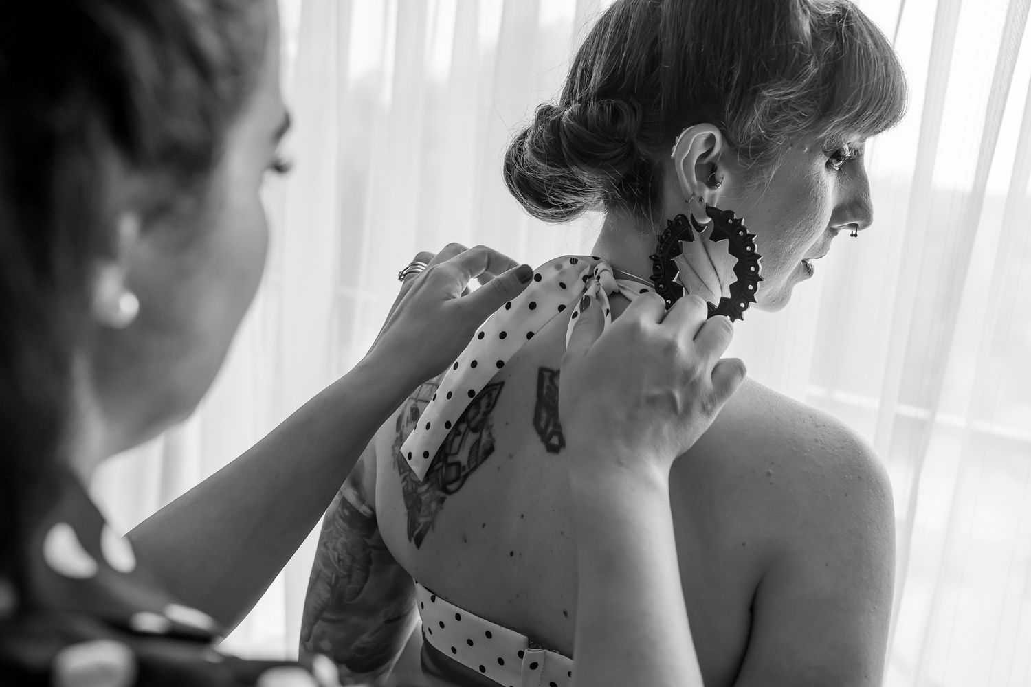 Black and white photo showing temporary henna tattoo being applied to someone's bare shoulder in soft window light.