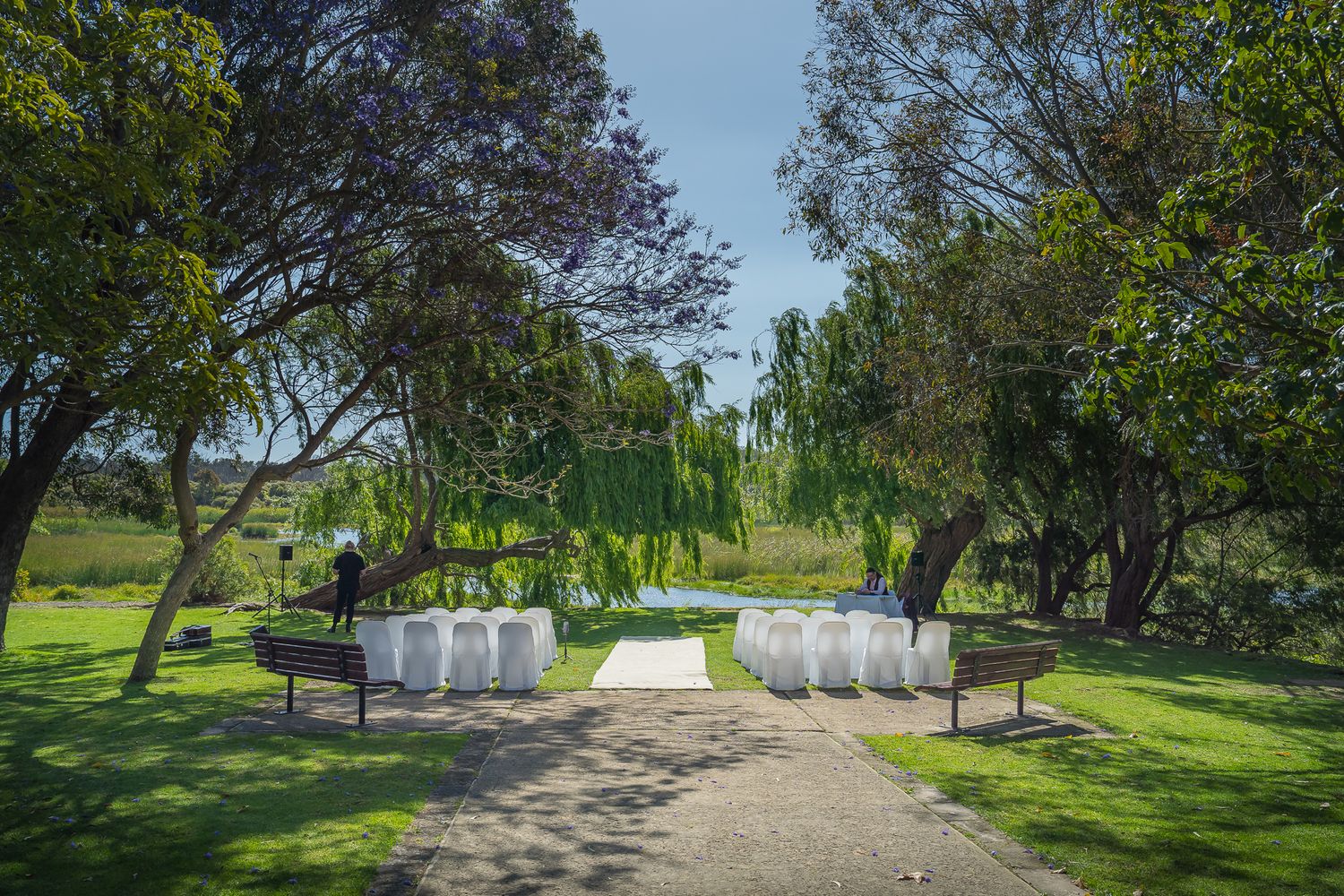 White chairs arranged on a garden path for an outdoor wedding ceremony under trees at a scenic venue.