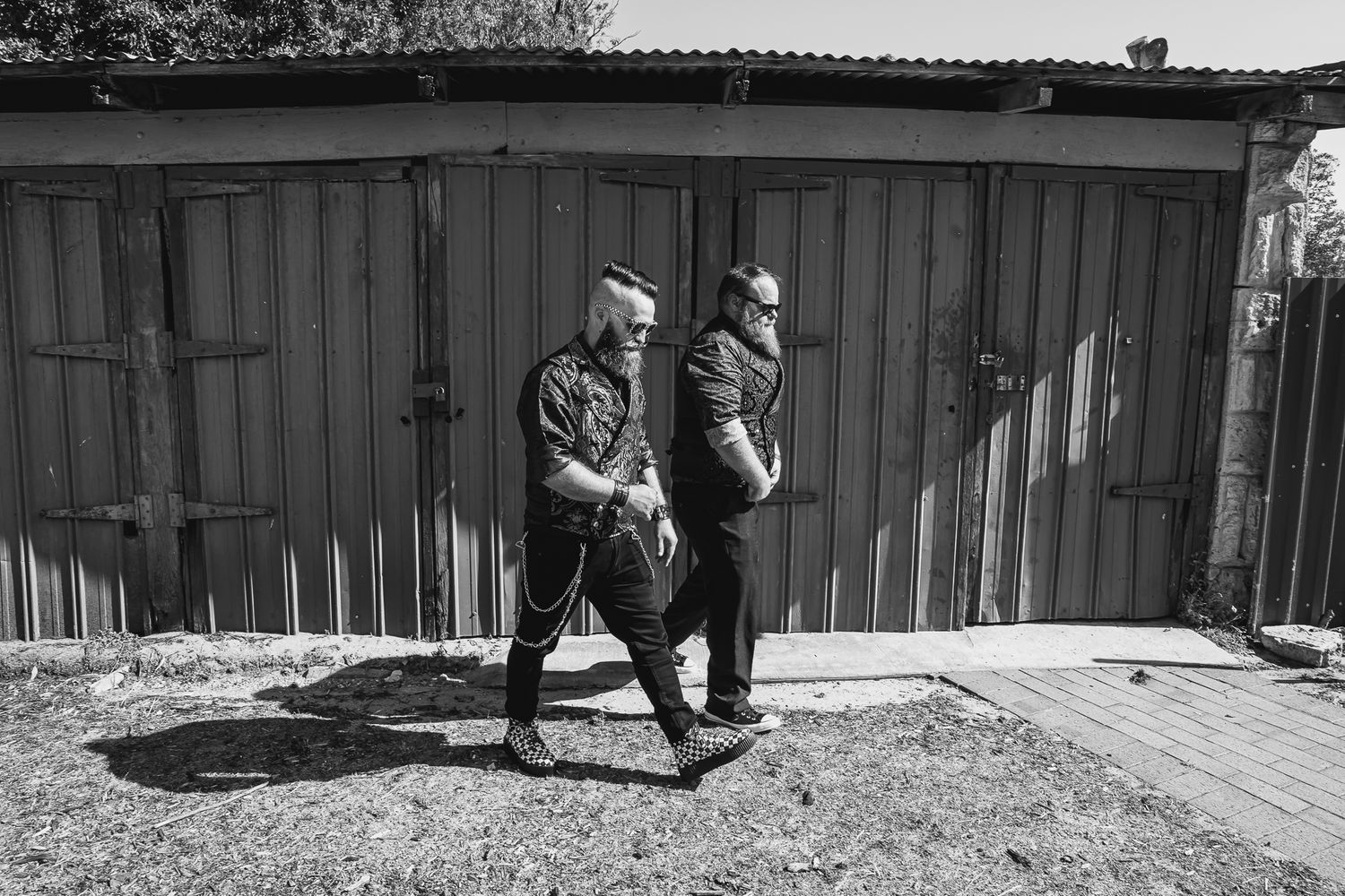 Two people walking past a row of wooden storage garages in black and white photography.