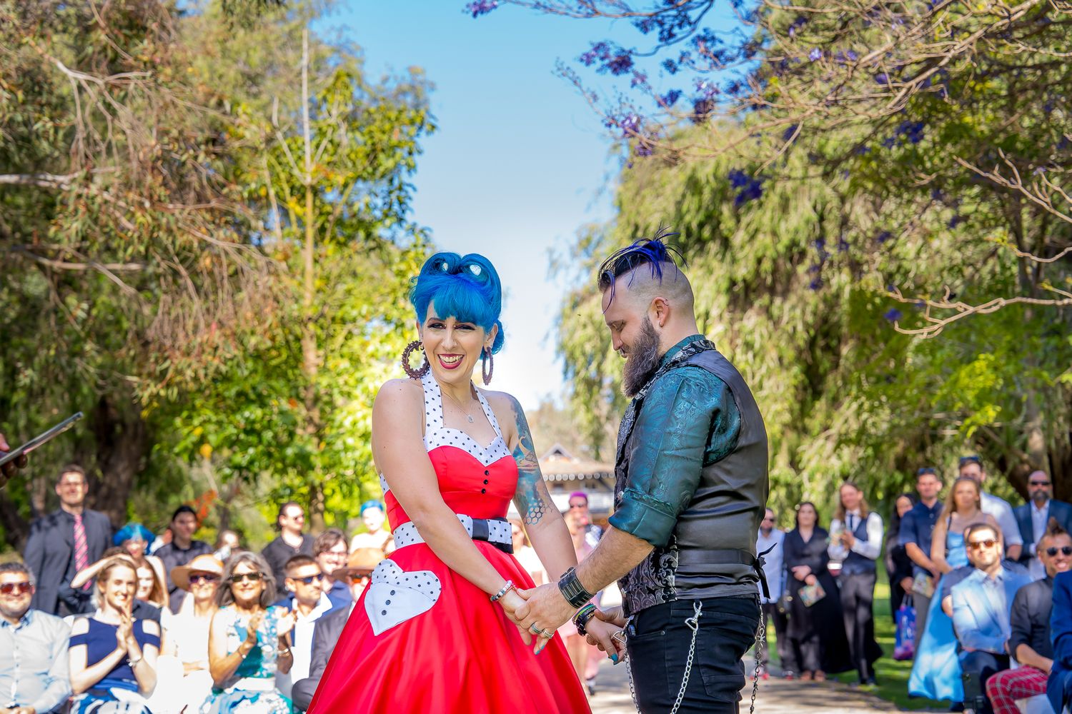 Two people share a special moment in a scenic outdoor garden setting surrounded by gathered guests.