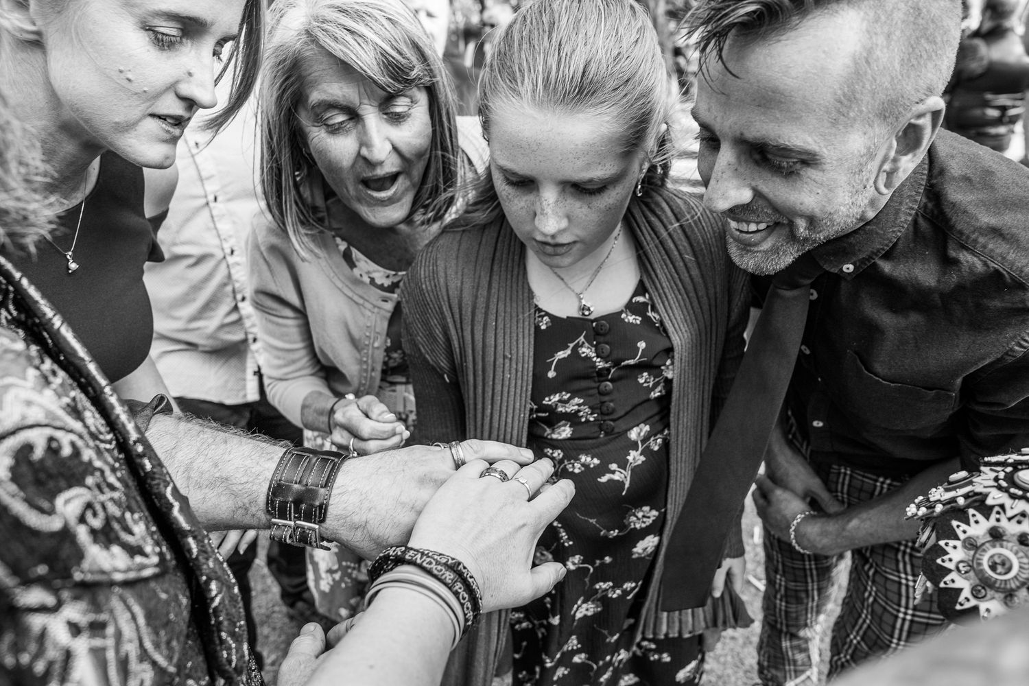 A small group of friends huddle together excitedly looking down at something in their hands in black and white.