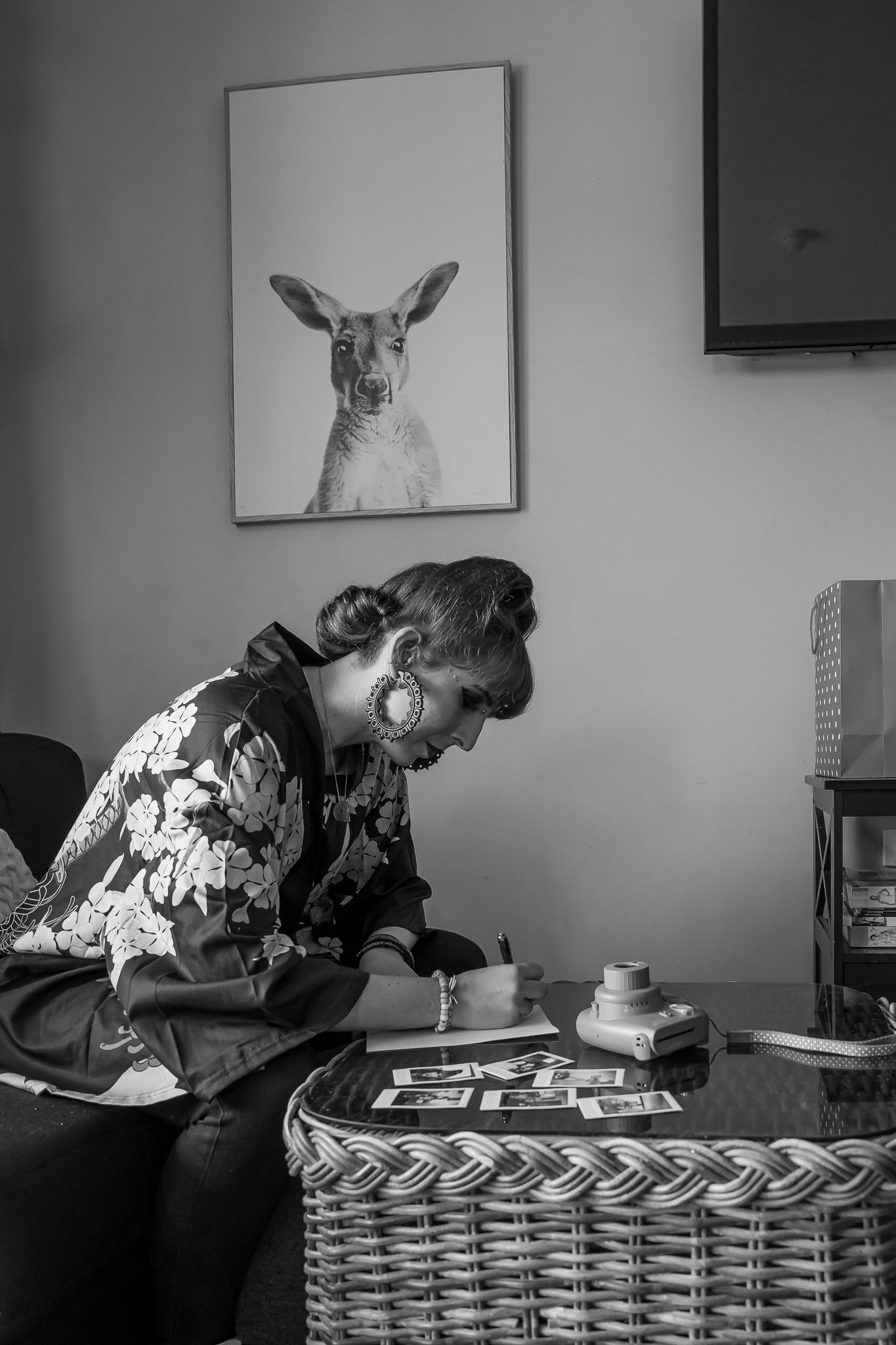 A person writes in a black and white photograph with a decorative kangaroo portrait hanging on the wall above.