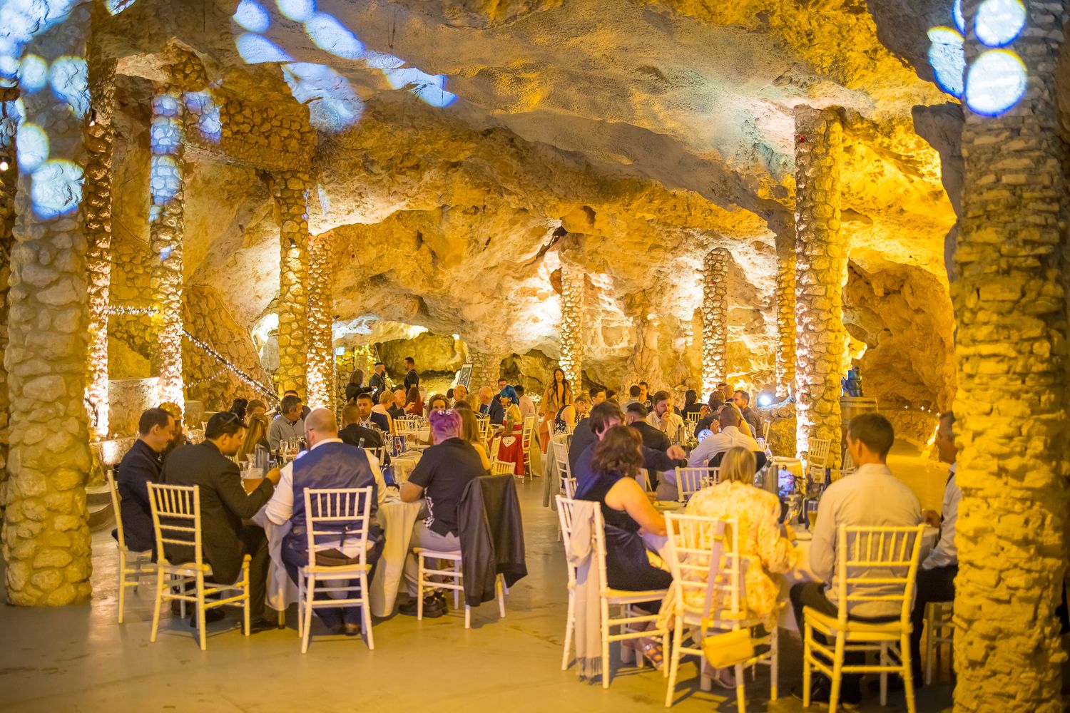 Wedding reception dinner in a romantic cave venue decorated with hanging string lights and elegant table settings.