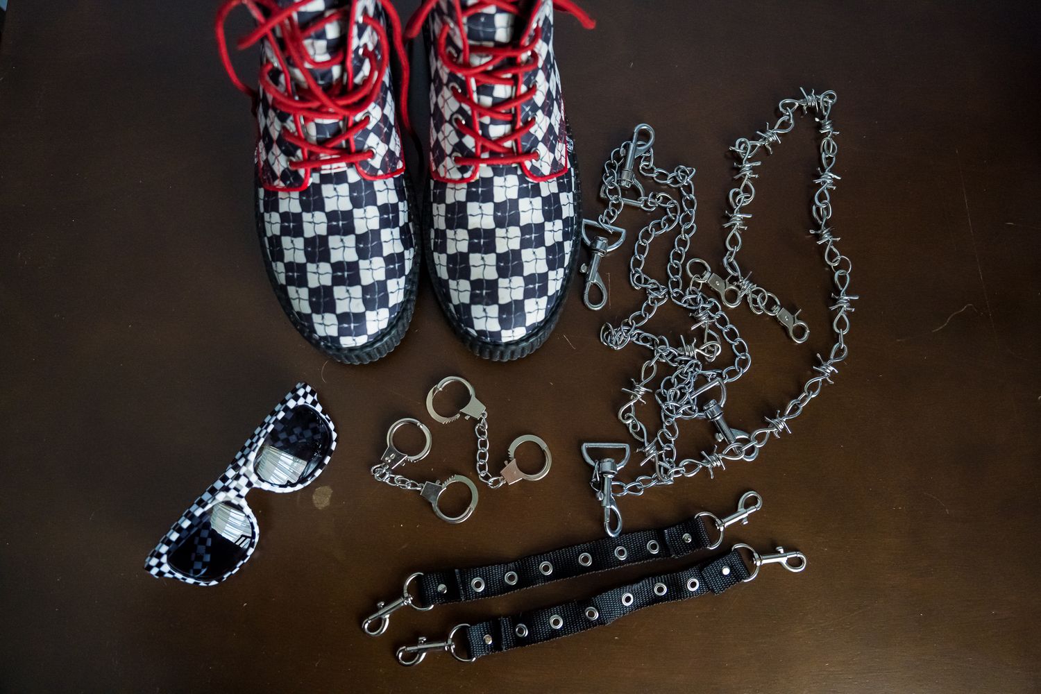 High contrast red and checkered Vans sneakers styled with sunglasses, chains and bracelet accessories on dark background.