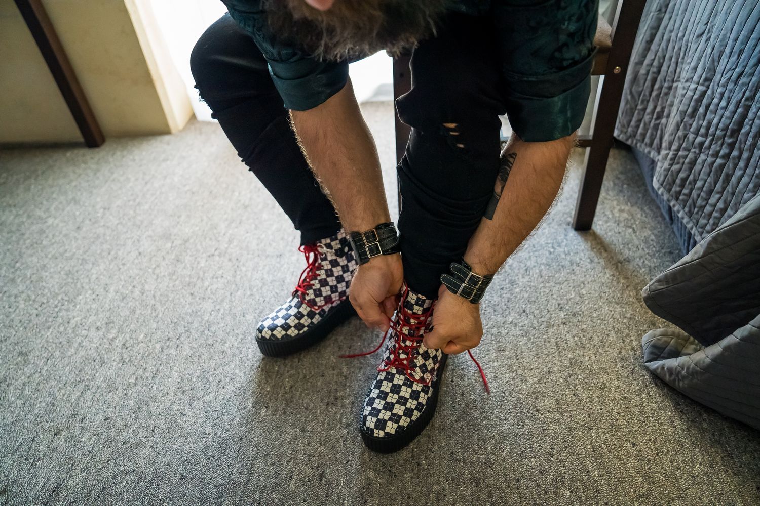 Someone tying the laces on a pair of black and white checkered slip-on Vans shoes on a carpeted floor.