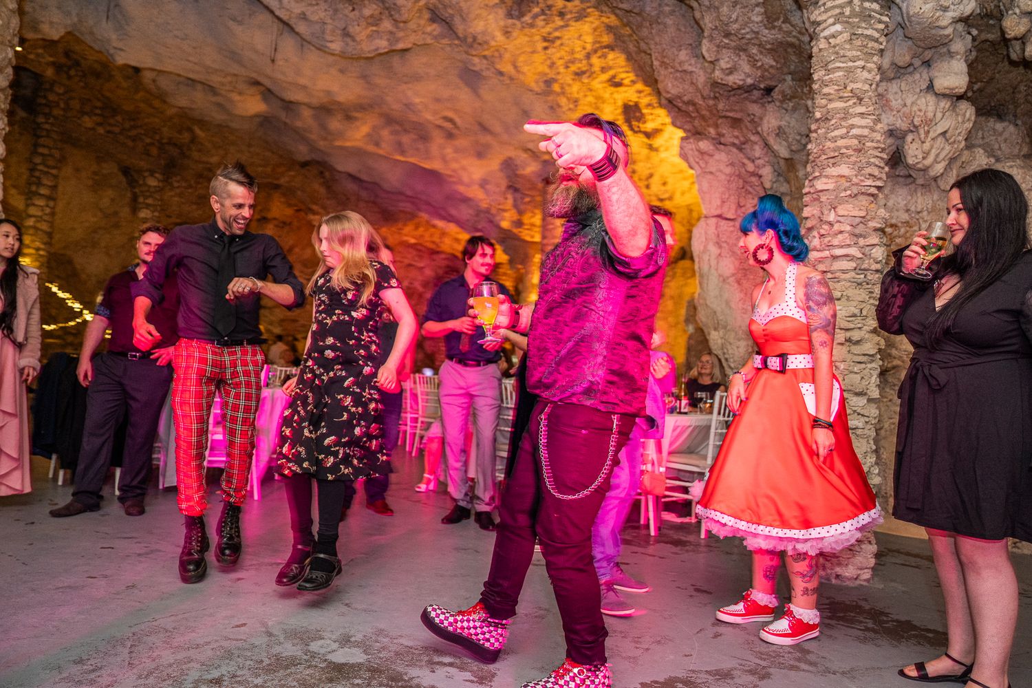 Dancers in vibrant red and pink outfits performing in an underground stone cavern with warm lighting.
