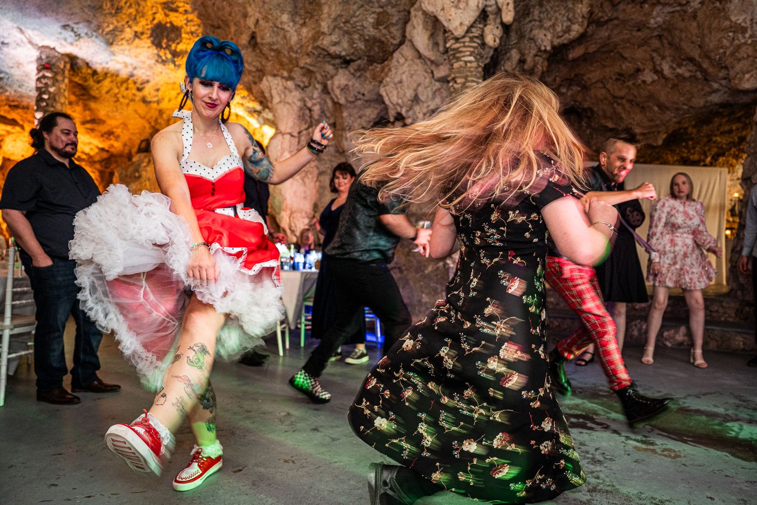 People dancing energetically in a cave-like venue with colorful lighting and festive outfits.