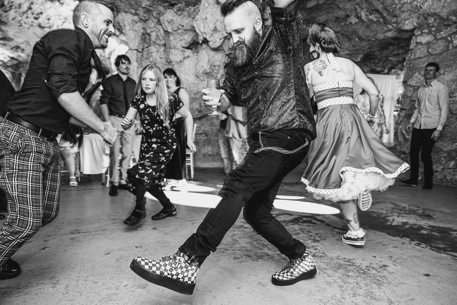 People dancing energetically in a rockabilly style at an underground venue with a black and white aesthetic.