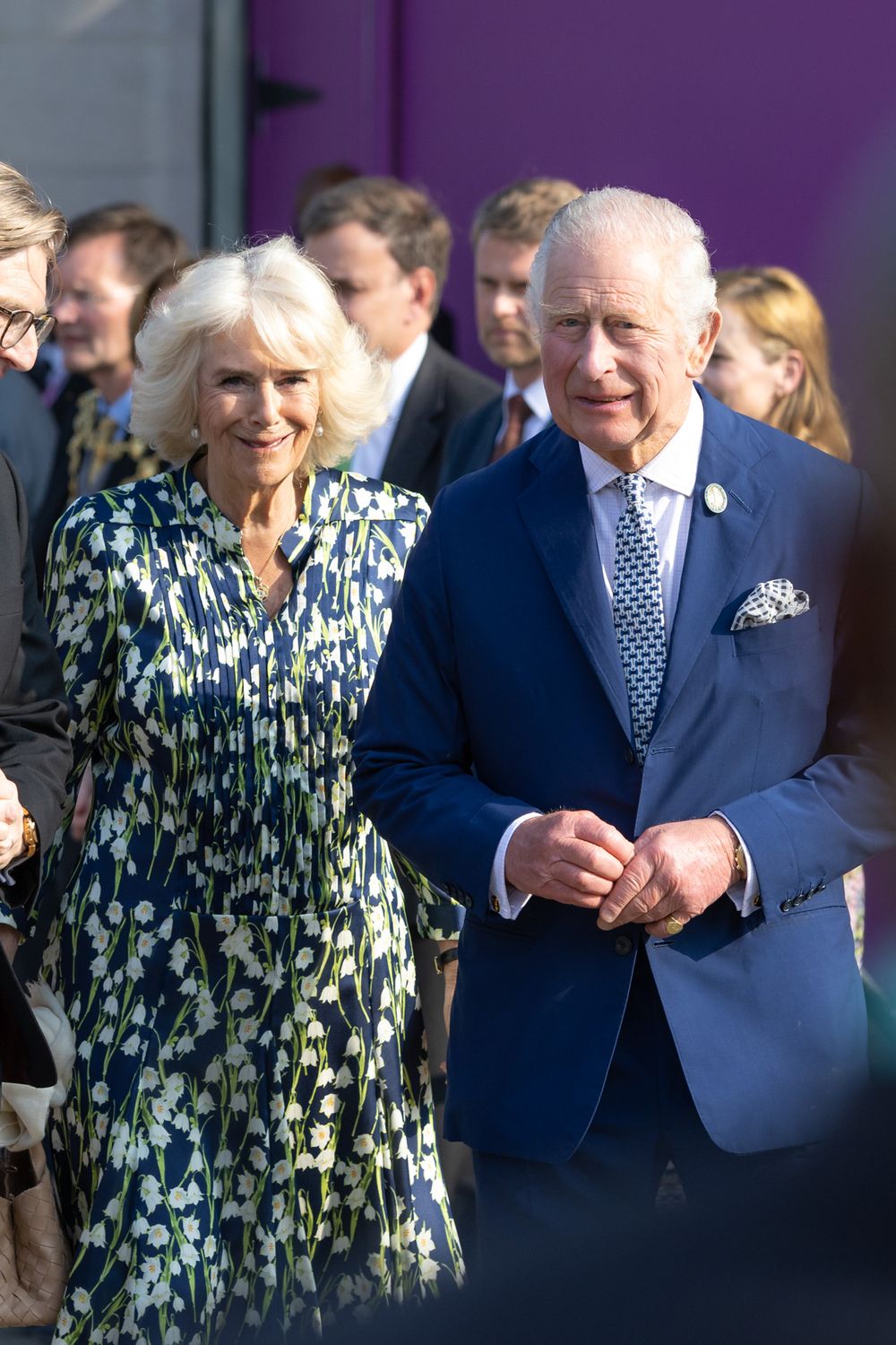 A couple dressed in formal attire walking together at an outdoor event.