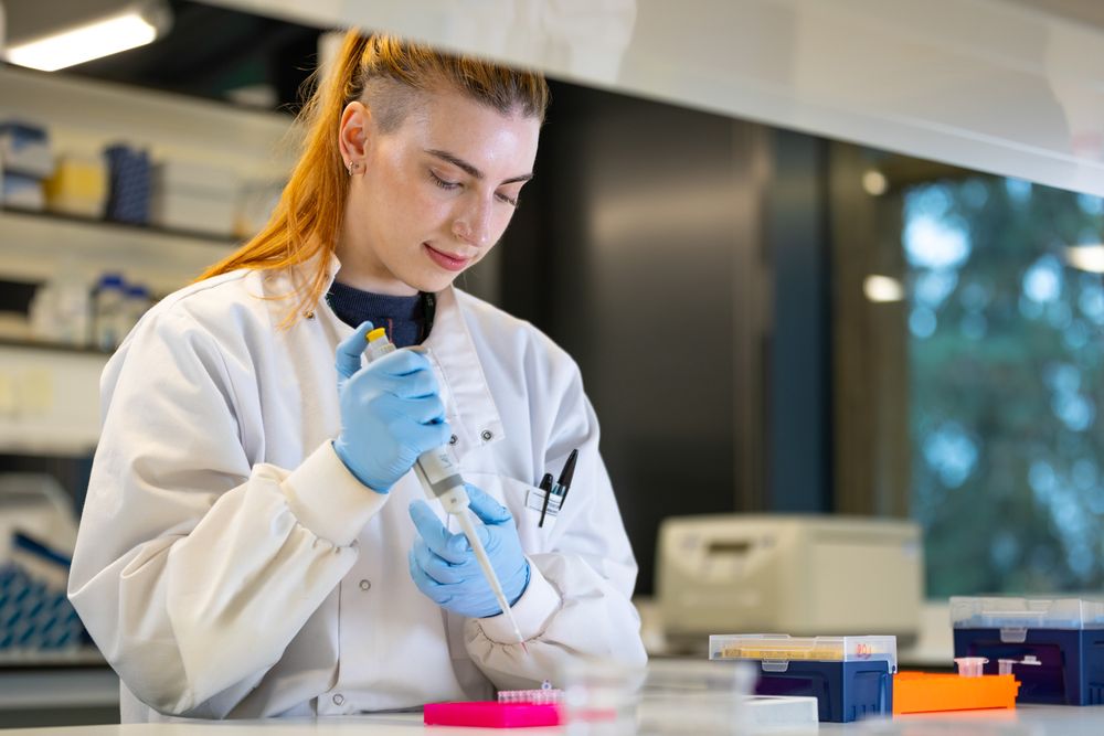 Scientist in protective gear handling laboratory equipment with colorful test tubes and supplies.