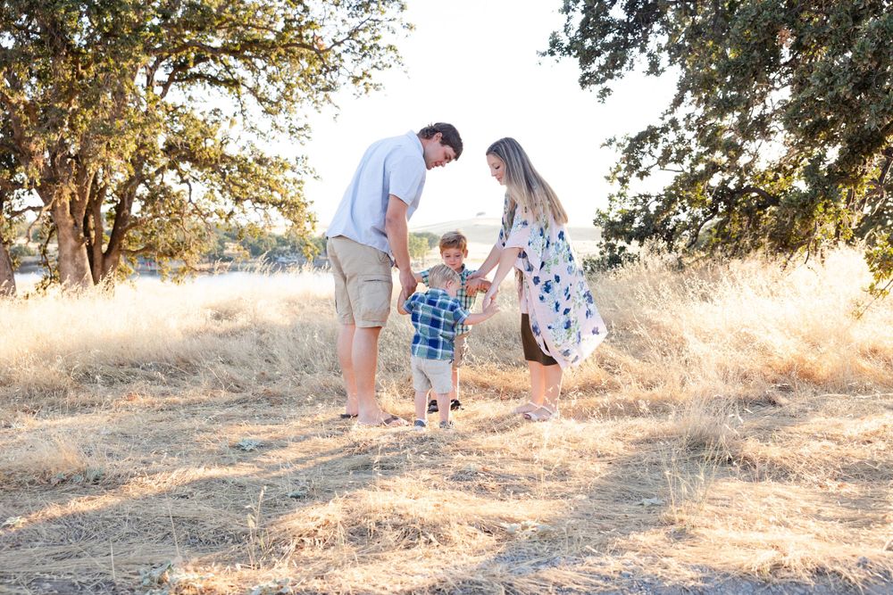Family playing together in dried grass field during golden hour photo session.