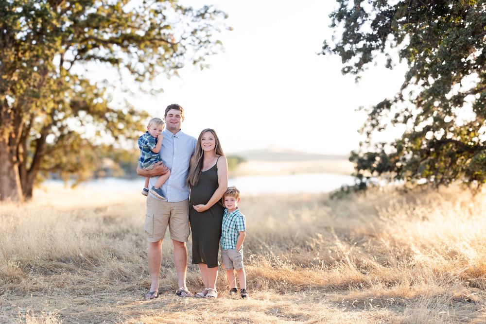 Family stands together in golden light on grassy hill during sunset portrait session.