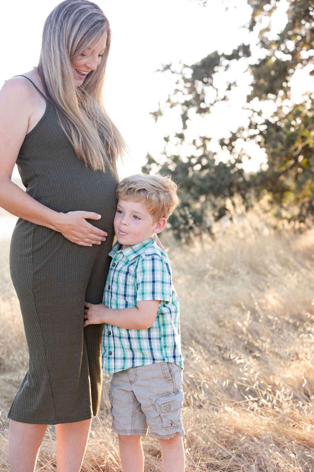 Mother and child share tender moment during maternity photo session in sunlit field.